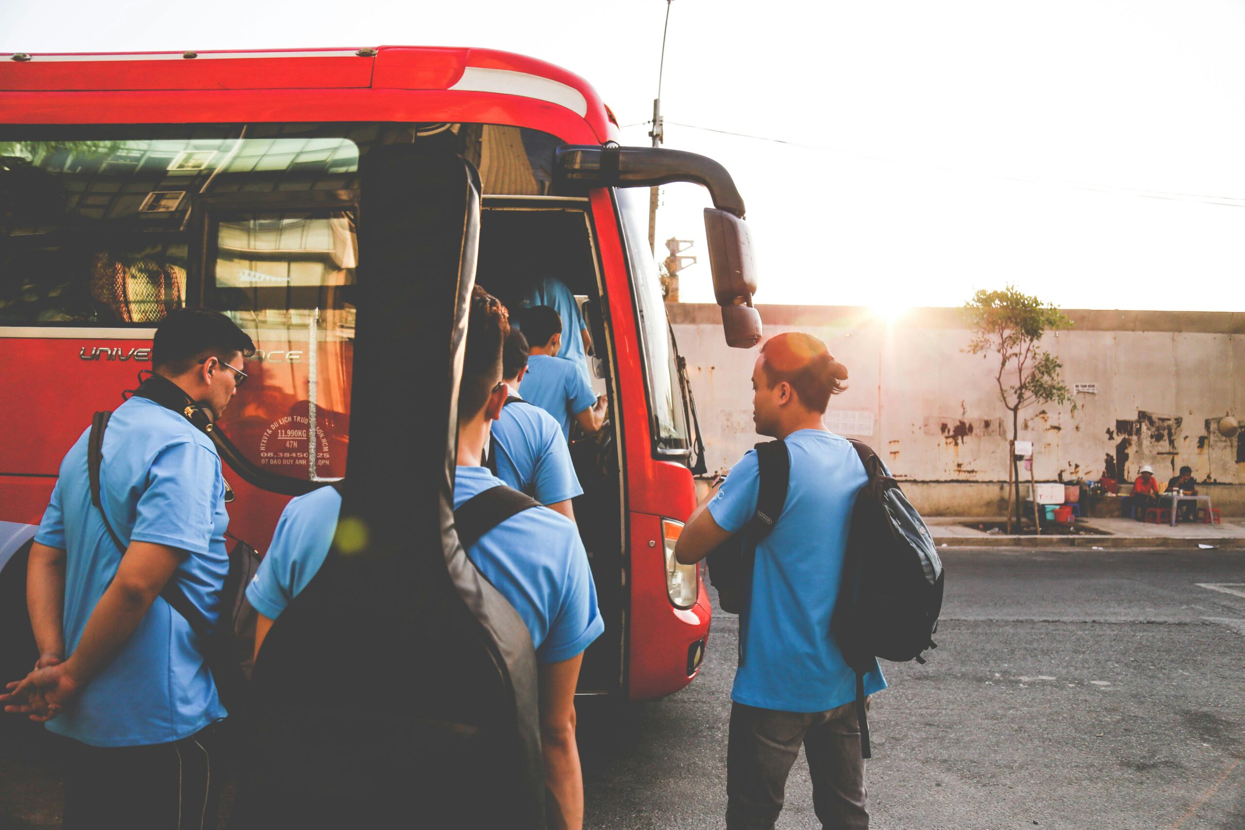 Musicians boarding a red bus in Tân Bình, Hồ Chí Minh City during sunrise. A lively street scene.
